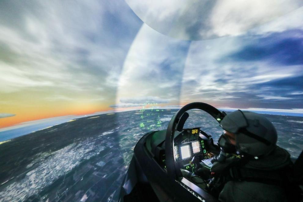 Pilot operating a sophisticated flight simulator with panoramic digital displays, showcasing defense innovation, aerospace technology, and strategic security capabilities within Europe’s critical technology sectors.