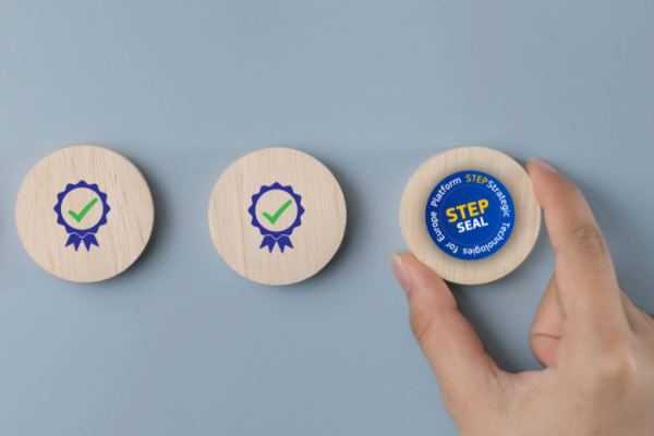 Three wooden discs, two with checkmark badges and one labeled “STEP Seal,” held by a hand.