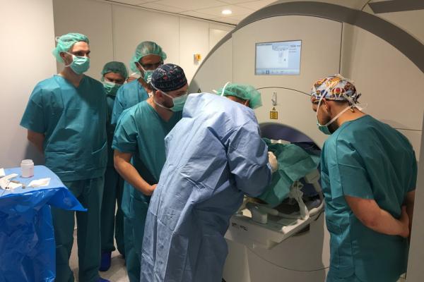 Group of surgeons in green scrubs and surgical caps gathered around a patient undergoing a procedure with a large medical imaging machine, demonstrating the precision and teamwork involved in gene therapy for Parkinson’s disease.